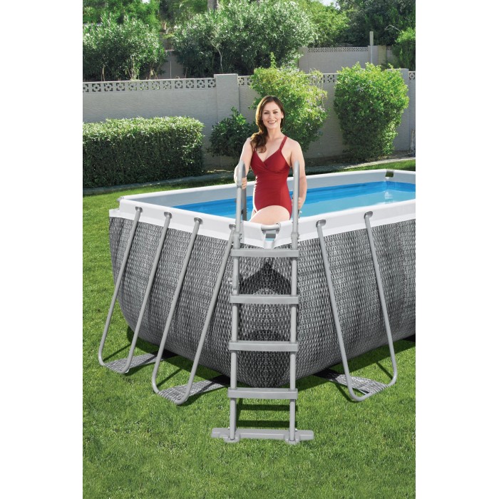Piscina fuori terra rettangolare con scaletta e donna in costume rosso in giardino.