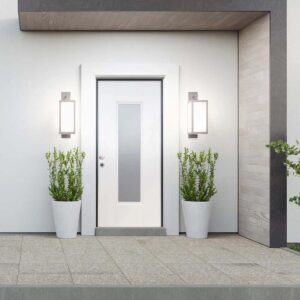 Porta blindata t.b.t. bianca con inserto in vetro, affiancata da luci esterne e piante.