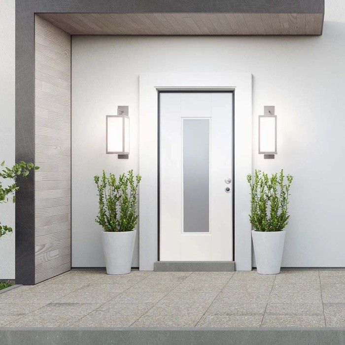 Porta blindata bianca con inserto in vetro, affiancata da due luci esterne e piante in vasi bianchi.