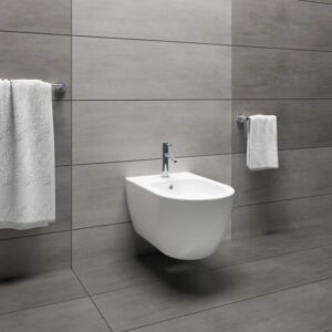 Bidet moderno sospeso in bianco con rubinetto su parete grigia.