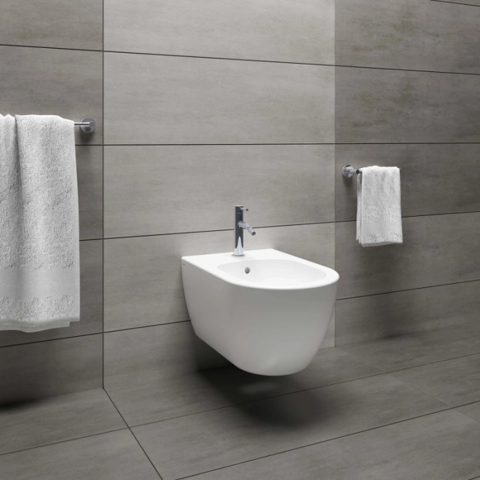Bidet moderno sospeso in bianco con rubinetto su parete grigia.