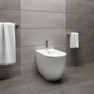 Bidet bianco moderno in bagno con piastrelle grigie e asciugamani.