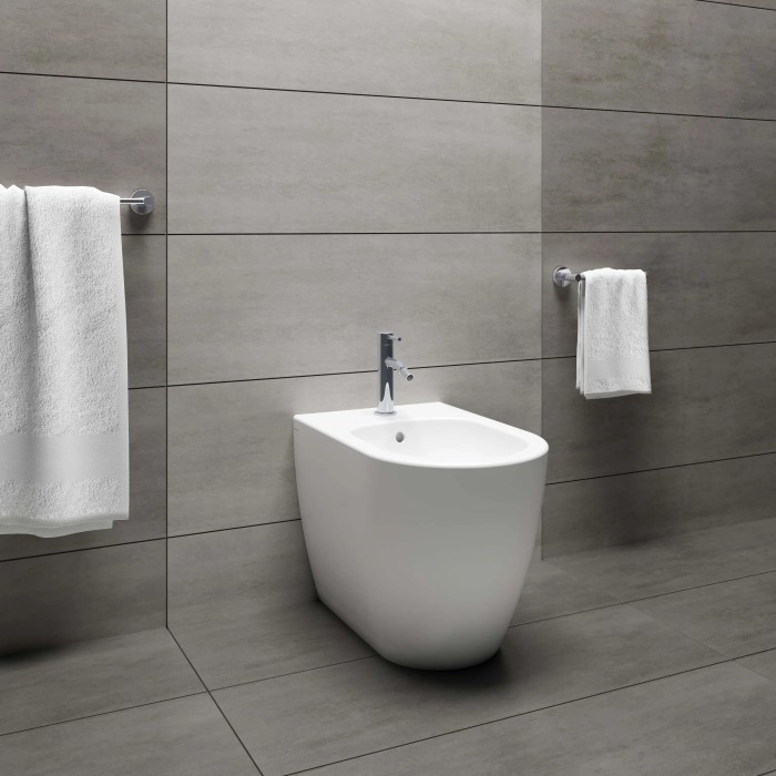 Bidet bianco moderno in bagno con piastrelle grigie e asciugamani.